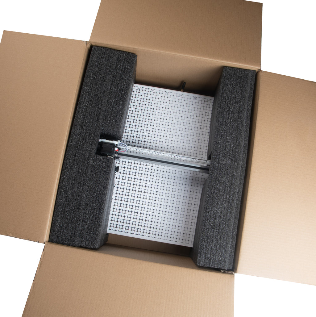 PaxieBot Plotter A3 machine. Cardboard box with a grid-like object inside, likely a filter or screen, on a white background.