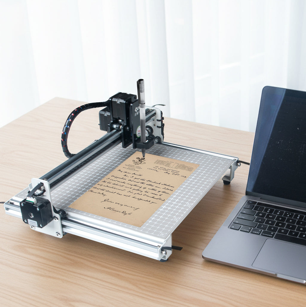 PaxieBot Smart Handwriting Machine on a table with a laptop next to it